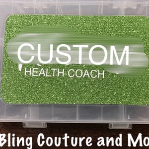 Puede incluir: Una caja de almacenamiento de plástico transparente con una tapa de purpurina verde. La tapa tiene una etiqueta blanca con el texto "CUSTOM HEALTH COACH".