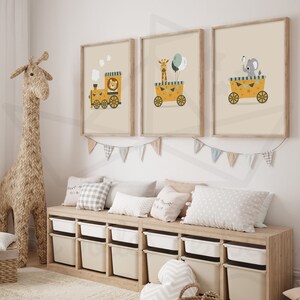 May include: Three framed illustrations of animals on a yellow train. The first illustration shows a lion, the second shows a giraffe, and the third shows an elephant. The illustrations are hung on a white wall above a wooden shelf with storage bins.