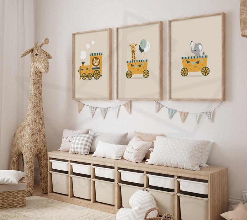 May include: Three framed illustrations of animals on a yellow train. The first illustration shows a lion, the second shows a giraffe, and the third shows an elephant. The illustrations are hung on a white wall above a wooden shelf with storage bins.