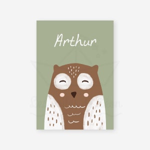 May include: A green card with the name "Arthur" written in white cursive. A brown owl with white spots and closed eyes is in the center of the card.