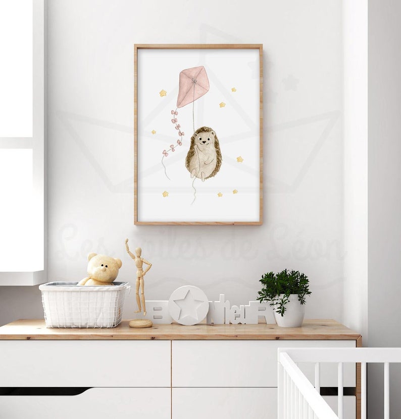 May include: A watercolour illustration of a hedgehog holding a pink kite with yellow stars in the background. The illustration is framed in a light wood frame.