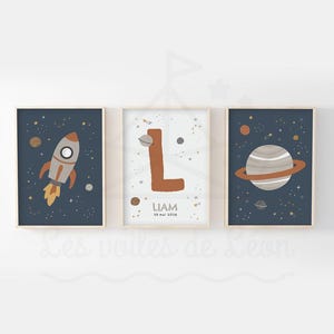 Peut inclure: Trois impressions d'art encadrées sur le thème de l'espace. L'une représente une fusée, une autre la lettre "L", et la troisième une planète avec des anneaux. Les fonds sont bleu foncé avec des étoiles et des planètes.