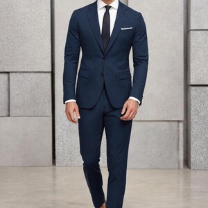 May include: A man wearing a dark blue suit with a white shirt and a black tie. He is wearing brown leather shoes.