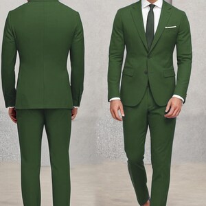 May include: A dark green suit with a single-breasted jacket and matching trousers. The jacket has a pocket on the left side and a button fastening. The suit is worn by a person with a white shirt and a dark green tie.