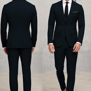 May include: A black suit with a single-breasted jacket and matching trousers. The jacket has a notch lapel and a pocket on the left side. The man is wearing a white shirt and a black tie.