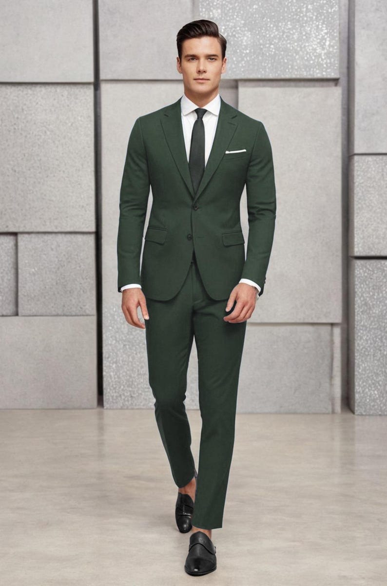 May include: A dark green suit with a white shirt and a dark tie. The suit jacket has a single button closure and a pocket on the left side. The man is wearing black shoes.