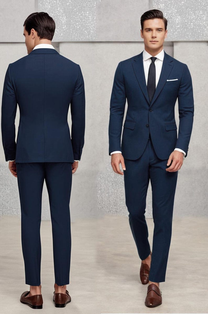 May include: A dark blue suit with a single-breasted jacket and matching trousers. The jacket has a pocket on the left side and a button fastening. The suit is worn by a person with brown hair and a white shirt with a dark blue tie.