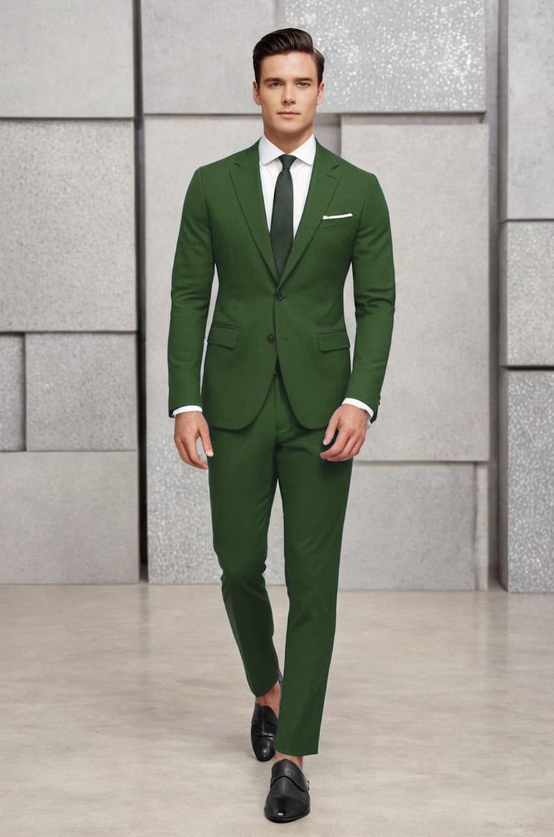 May include: A dark green suit with a white shirt and a dark green tie. The suit jacket has a single button closure and a pocket on the left side. The man is wearing black shoes.