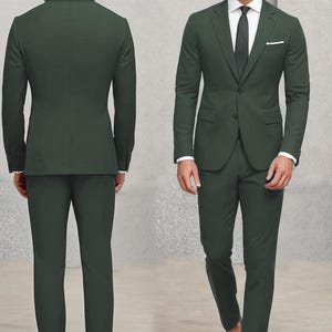 May include: A dark green suit with a single-breasted jacket and matching trousers. The jacket has a pocket on the left side and a button fastening. The suit is worn by a person with a white shirt and a dark tie.
