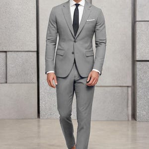 May include: A man wearing a grey suit with a white shirt and a dark grey tie. He is wearing brown leather shoes.
