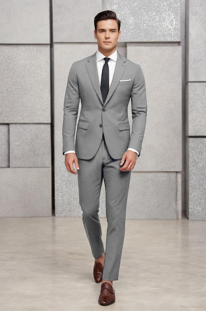 May include: A man wearing a grey suit with a white shirt and a dark grey tie. He is wearing brown leather shoes.