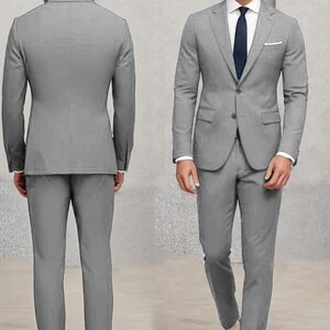 May include: A grey suit with a single-breasted jacket and matching trousers. The jacket has a pocket on the left side and a button fastening. The suit is worn by a person with brown hair and a white shirt with a dark blue tie.