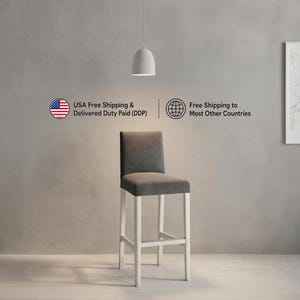 May include: A bar stool featuring a dark gray upholstered seat and backrest supported by a white wooden frame with four legs and a footrest. The stool is positioned centrally in the frame, showcasing a clean, structured design with a high back.