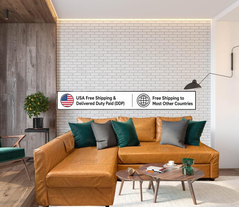 Op de afbeelding: Een beige lederen hoekbank met een chaise longue, voorzien van donkergroene en grijze sierkussens. Voor de bank staan twee houten salontafels. Een witte bakstenen muur vormt de achtergrond voor deze meubelopstelling in de ruimte.
