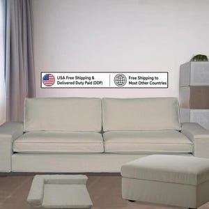 Puede incluir: Un sofá de color beige claro con dos cojines de respaldo grandes y dos cojines de asiento, acompañado de un reposapiés rectangular a juego y una cama pequeña para mascotas. El conjunto presenta una tapicería de tela neutra y diseño simple.