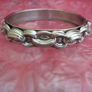 May include: A silver bangle bracelet with a decorative design of overlapping waves.