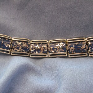 May include: A gold and blue bracelet with a repeating pattern of silver glitter. The bracelet is made of metal and has a hinged clasp.
