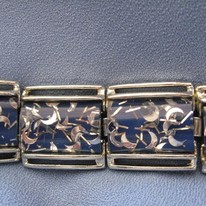 May include: A silver bracelet with a blue background and silver glitter. The glitter is shaped like crescent moons.