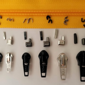 Peut inclure: Assortiment de tirettes et de curseurs de fermeture éclair en argent, noir et or. Les tirettes de fermeture éclair sont marquées "YKK".