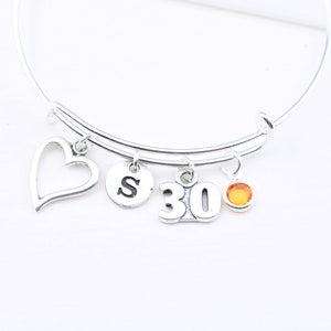 May include: Silver charm bracelet with a heart, letter 'S', number '30', and a small orange stone charm.