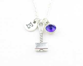 May include: Silver necklace with a charm of a hammer, a purple crystal, and a silver disc with the letter 'E' engraved on it.