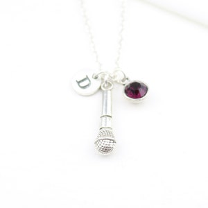 Op de afbeelding: Zilveren ketting met een microfoonbedel, een kleine ronde paarse edelsteen en een zilveren bedel met de letter "D" erop.