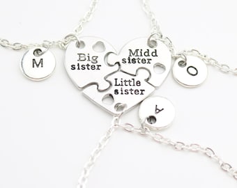 May include: Three silver bracelets with heart-shaped puzzle pieces that say "Big sister", "Middle sister", and "Little sister". Each bracelet has a small round charm with a letter on it.