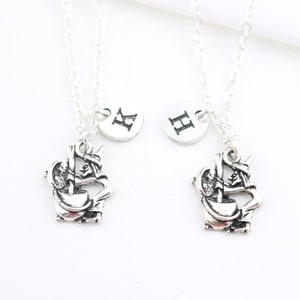 Peut inclure: Deux colliers en argent avec des pendentifs assortis. Chaque pendentif représente une image stylisée d'une licorne. Les colliers ont un disque en argent avec les lettres "K" et "H" gravées dessus.