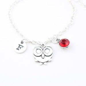 Puede incluir: Un brazalete de plata con un dije de búho, un dije de cristal rojo y un dije con la letra "F".