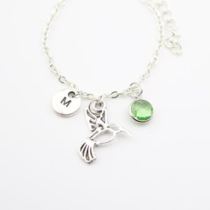 Può includere: Un braccialetto a catena d'argento con un ciondolo a forma di colibrì, un ciondolo di pietra preziosa verde e un ciondolo d'argento con la lettera "M" sopra.