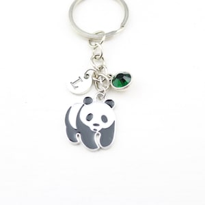 May include: Silver keychain with a panda bear charm, a green gemstone, and a small initial charm. The panda is black and gray with a white background. The keychain is on a white background.
