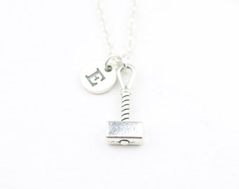 May include: Silver necklace with a small silver hammer charm and a round silver charm with the letter E engraved on it.