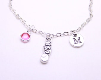 Könnte beinhalten: Silberne Kettenarmband mit drei Anhängern: einem rosa Kristall, einem silbernen Anhänger mit der Zahl "26,2" und einem silbernen Anhänger mit dem Buchstaben "M".
