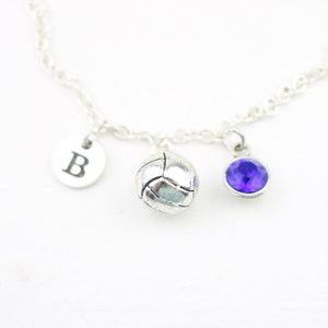 May include: Silver chain necklace with three charms: a volleyball, a letter 'B' charm, and a purple gemstone.