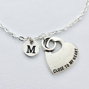Könnte beinhalten: Ein silbernes Kettenarmband mit einem Herz-Anhänger, auf dem "Close to my heart" steht, und einem kleinen Anhänger mit dem Buchstaben "M".