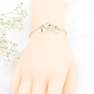 May include: A silver bracelet with a charm of two interlocking circles and a small heart charm. The bracelet also has a charm with the letter "K" on it.