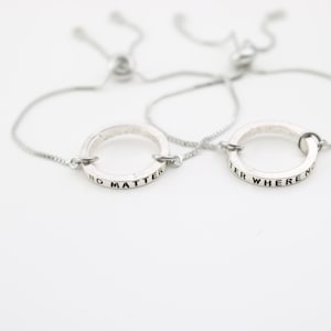May include: Two silver friendship bracelets with adjustable cords. One bracelet has the inscription "No Matter" and the other has the inscription "Where We Go".