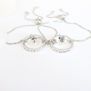 May include: Two silver friendship bracelets with adjustable cords. One bracelet says "Our Best Friends" and the other says "Friends Forever". Each bracelet has a small circle charm with a letter, "J" and "D", hanging from it.
