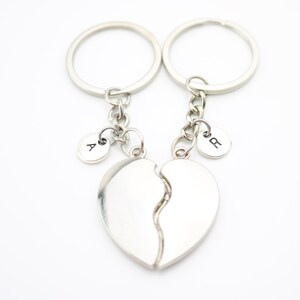 May include: Two silver keychains with split heart charms and letter charms. The charms are engraved with the letters "A" and "B".