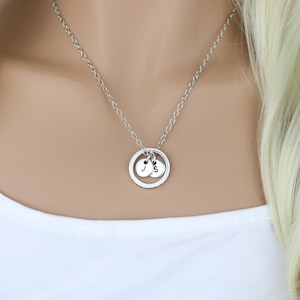 Puede incluir: Un collar de plata con un colgante circular y dos pequeños dijes con las letras "J" y "S" colgando.