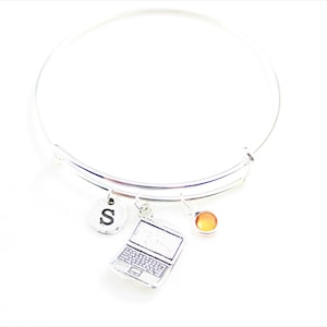 May include: A silver charm bracelet with a laptop charm, a letter 'S' charm, and an orange gemstone charm.