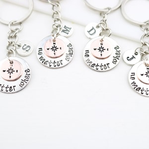 May include: Four silver keychains with compass charms and the words "no matter where" engraved on each. Each keychain also has a small silver charm with a letter on it.