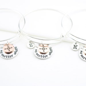 May include: Three silver charm bracelets with a compass charm and the words "no matter where" engraved on each charm. Each bracelet also has a letter charm.