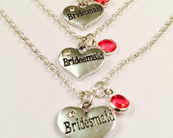 Peut inclure: Trois colliers en argent avec des pendentifs en forme de cœur qui disent "Bridemaid" et ont un petit charme en strass rouge.