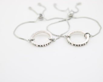 May include: Two silver friendship bracelets with adjustable cords. One bracelet has the inscription "No Matter" and the other has the inscription "Where We Go".