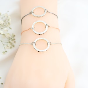 Könnte beinhalten: Drei silberne Armbänder mit einem Kreisanhänger, auf dem jeweils "Whatever" steht. Die Armbänder befinden sich am Handgelenk einer Person.