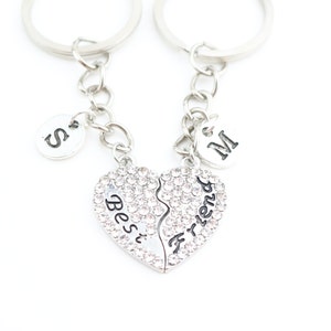 May include: Two silver keychains with a heart-shaped charm that says "Best Friend" in black lettering. The charms are split in half and each half has a small silver charm with a letter on it. One charm says "S" and the other says "M".