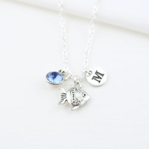 May include: Silver necklace featuring a blue crystal, a fish charm, and a round charm with the letter "M" on it.
