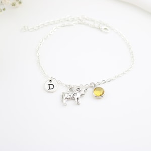 May include: A silver charm bracelet featuring a cow charm, a yellow crystal charm, and a silver charm with the letter D.