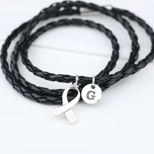 May include: A black leather braided bracelet with a silver ribbon charm and a silver charm with the letter "G" engraved on it.